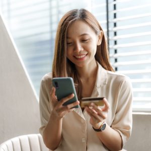 Young pretty asian female using credit card to do online product shopping on her mobile, cashless concept.